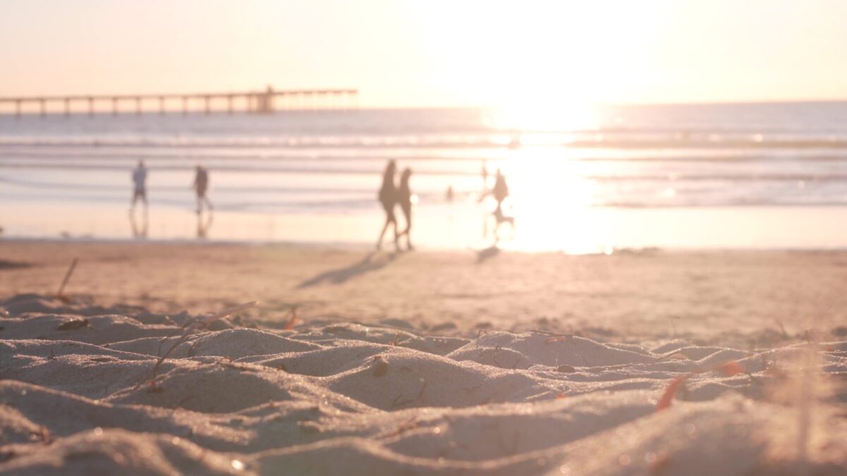 people walking on sandy ocean beach by pier at sunset, california coast, usa.